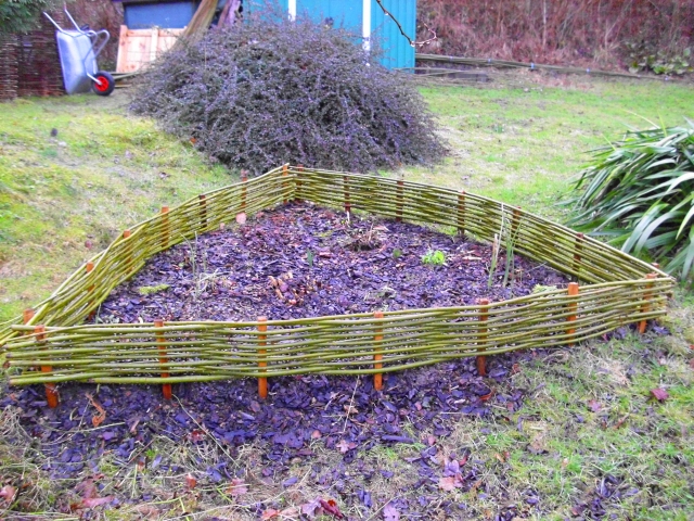 3-eckige Beeteinfassung aus Weidenruten mit Holzpflöcken, Rindenmulch in der Mitte